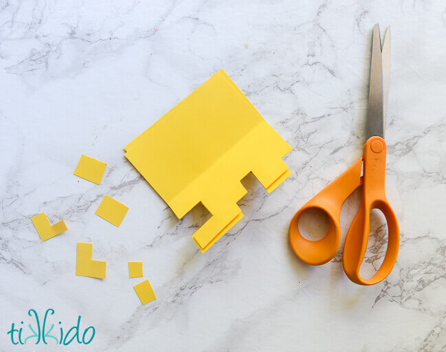 Yellow paper being cut into life sized pixelated Minecraft flowers for a Minecraft birthday party.