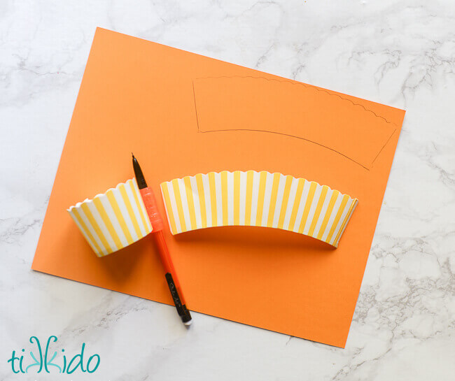 Tracing the shape of cupcake wrappers on a piece of orange paper.