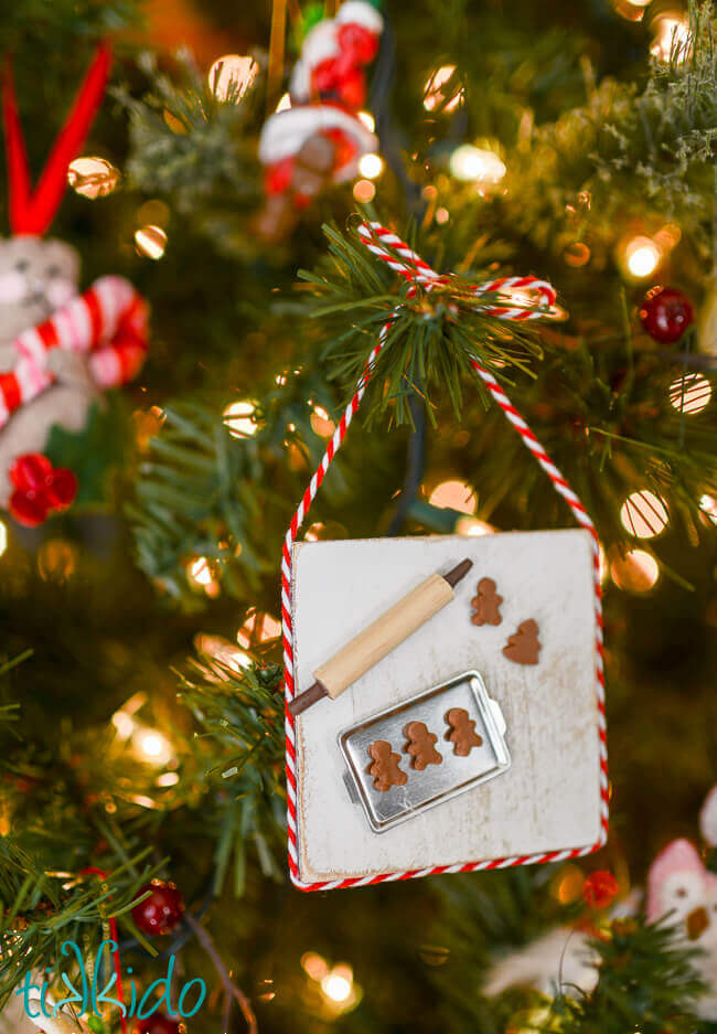 Christmas ornament that looks like a miniature baking scene with a tiny pan, rolling pin, and gingerbread cookies.