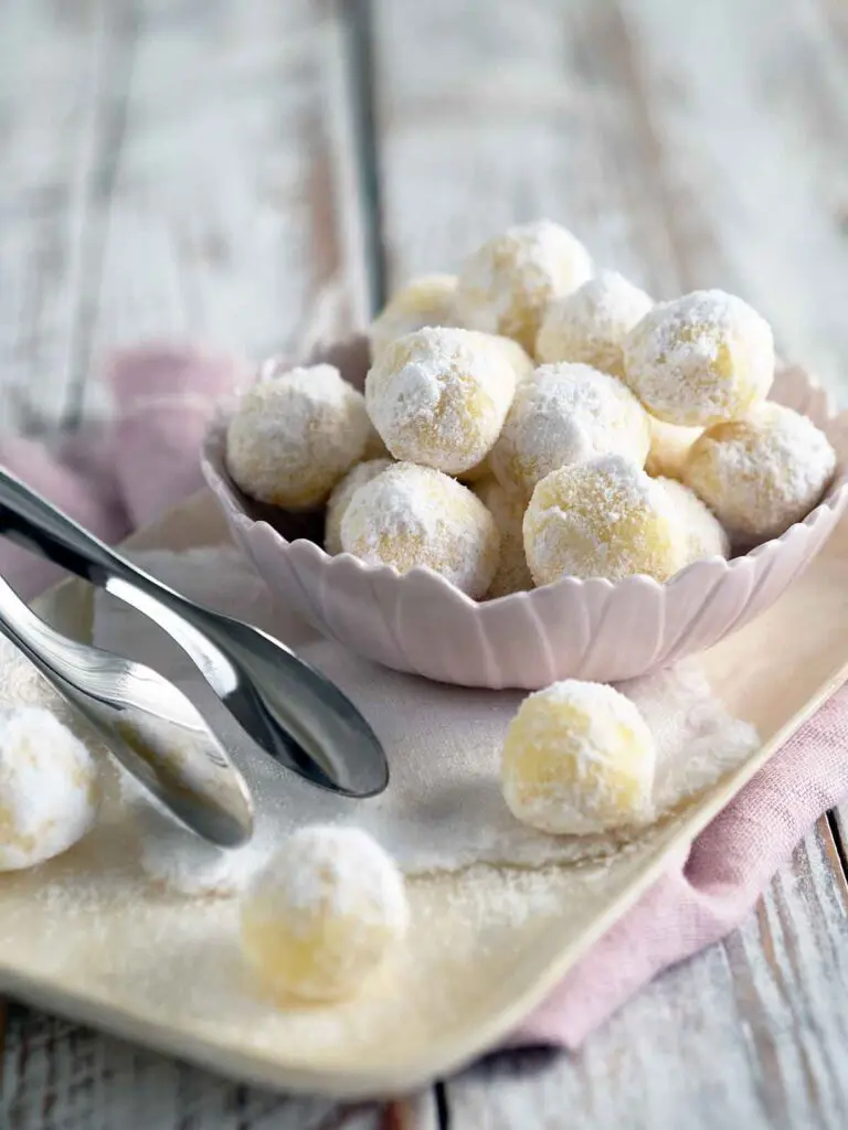 Light pink bowl of white chocolate mint truffles on a serving tray next to a pair of silver tongs.