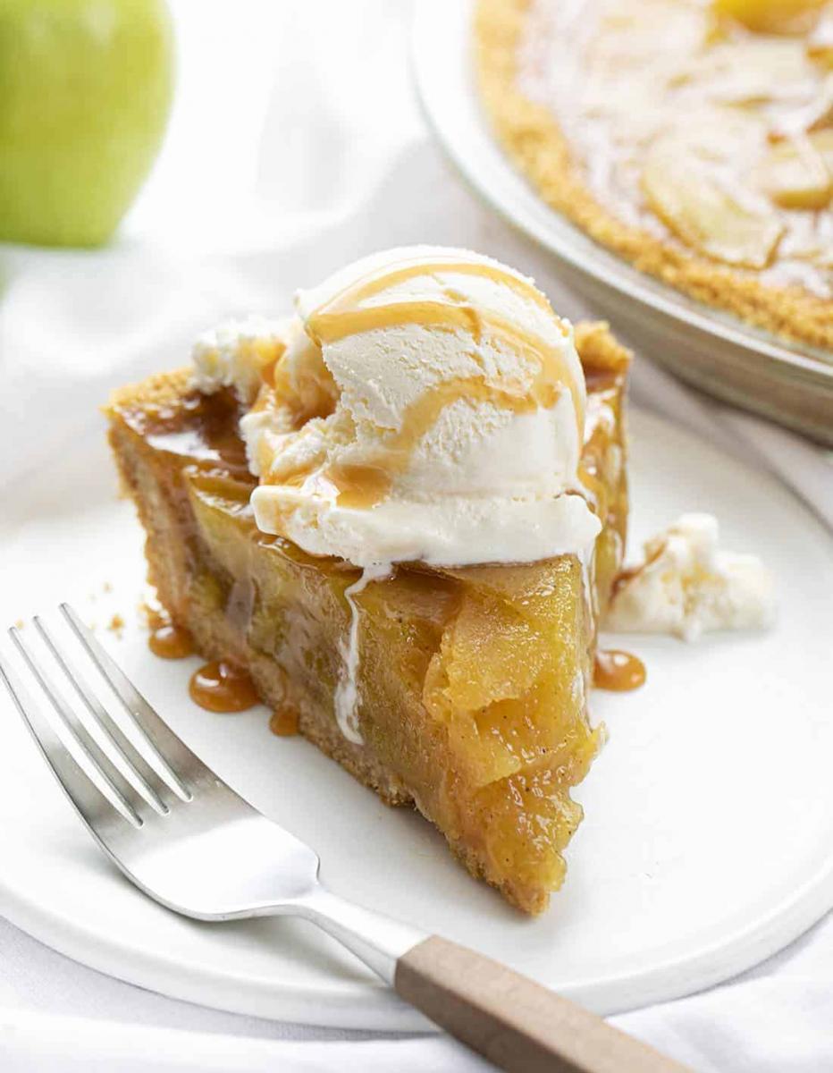 A slice of no bake apple pie topped with a scoop of vanilla ice cream and drizzled with caramel syrup on a white plate.