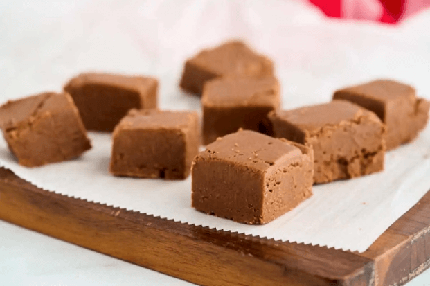 Pieces of old fashioned fudge on parchment paper on a wooden cutting board.