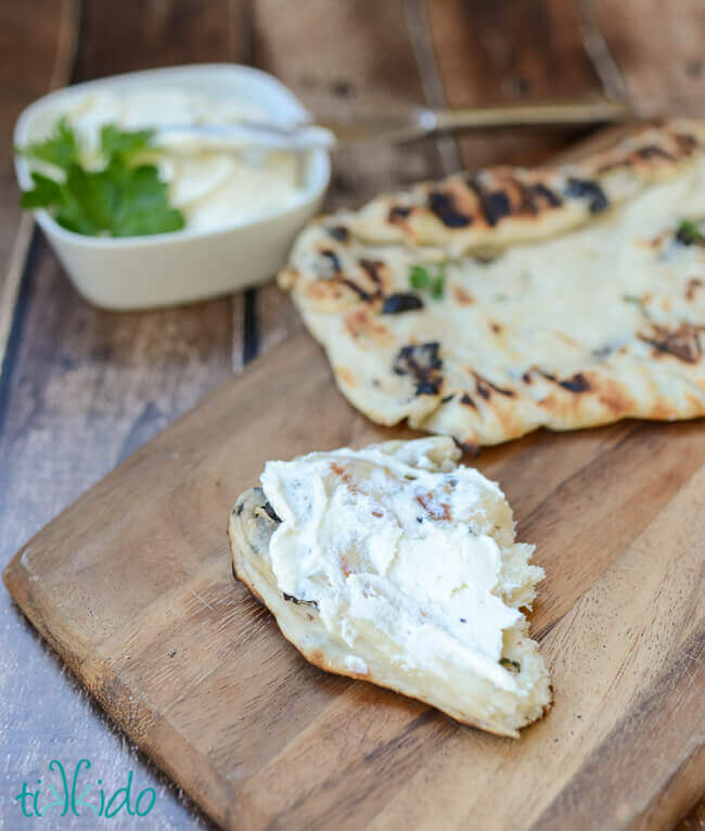 Torn piece of grilled bread spread with whipped feta spread, on a wooden cutting board.