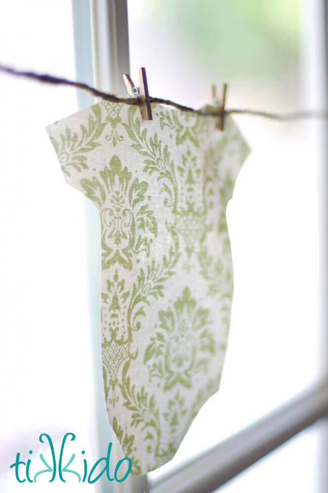 Fabric cut into a baby's onesie shape and hung with miniature clothespins to make a Baby Shower Garland
