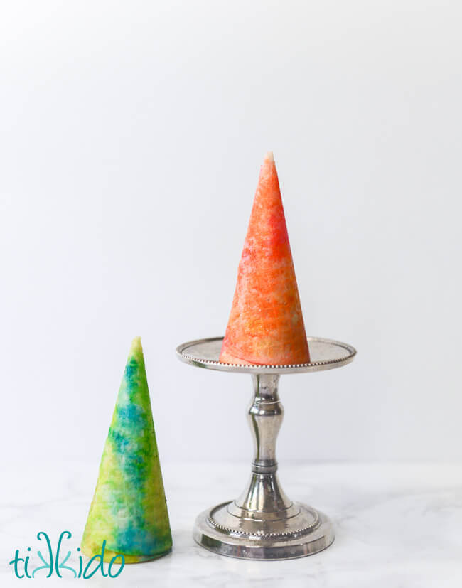 Two edible painted ice cream cones, one in orange and pink colors, one in blue and green colors.