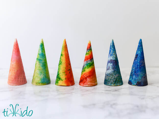 Six ice cream cones painted with food coloring with watercolor techniques, on a white background.