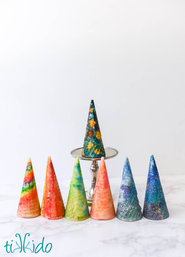 Seven ice cream cones painted with food coloring with watercolor techniques, on a white background.