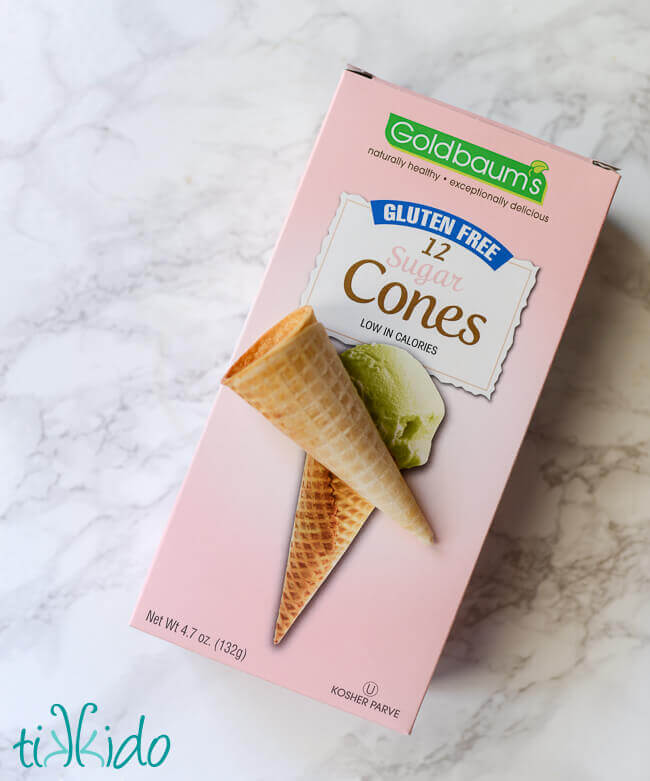 Box of gluten free ice cream cones, one cone out of package and on top of box, on a white marble surface.