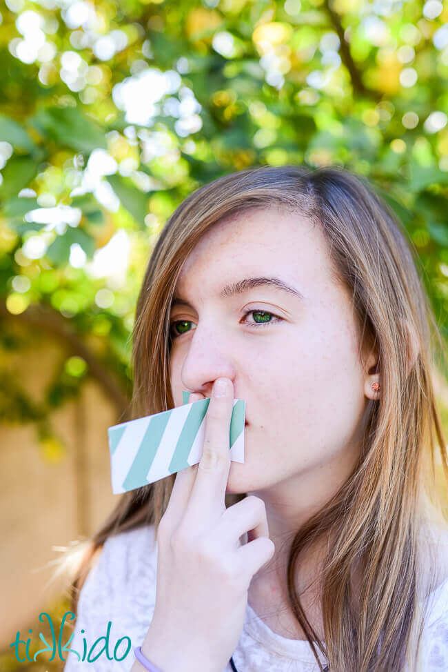 Girl using an easy paper noisemaker made from a strip of paper.
