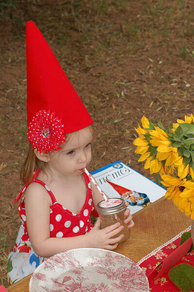 Little girl wearing a gnome hat and sipping a drink with a straw.