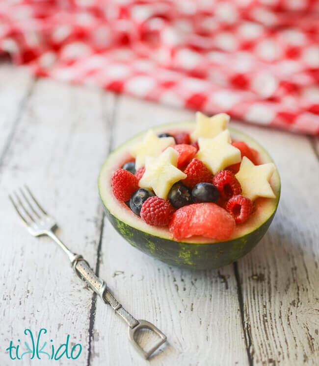 Small watermelon bowl full of raspberries, blueberries, watermelon, and apples cut into star shapes, for a 4th of July Fruit Salad.