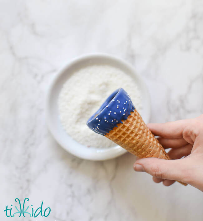 Ice cream cone edged in blue chocolate melts with white sprinkles.
