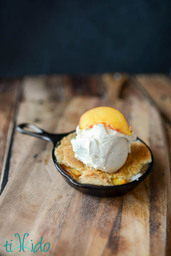 Homemade peach cobbler baked in a cast iron skillet and topped with a scoop of vanilla ice cream.