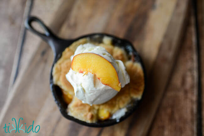 Homemade peach cobbler baked in a cast iron skillet and topped with a scoop of vanilla ice cream.