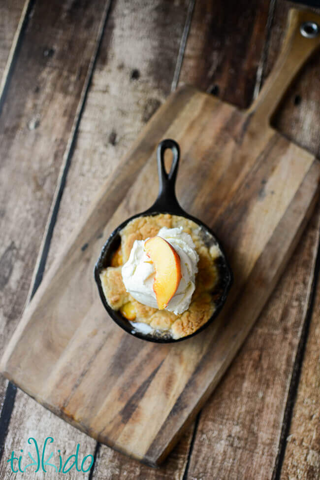 Homemade peach cobbler baked in a cast iron skillet and topped with a scoop of vanilla ice cream.