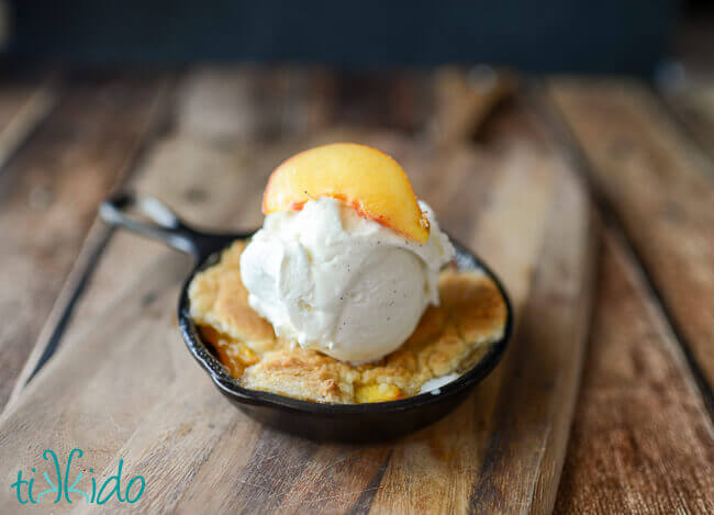 Homemade peach cobbler baked in a cast iron skillet and topped with a scoop of vanilla ice cream.