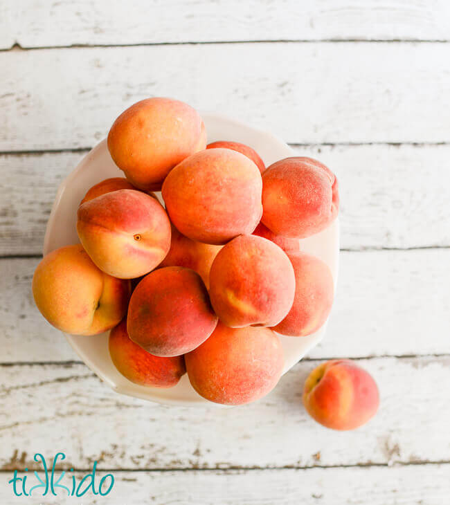 peaches in a white bowl on a white weathered wood background.