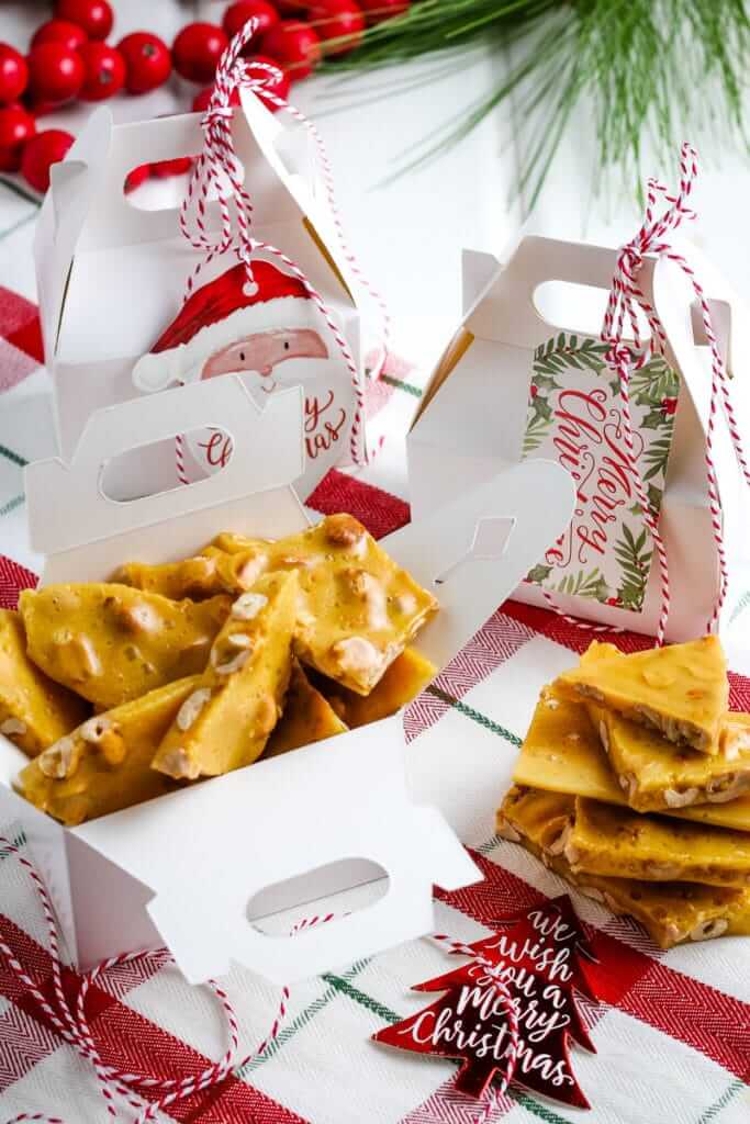 Homemade peanut brittle in white gift boxes tied with baker's twine and Christmas gift tags.