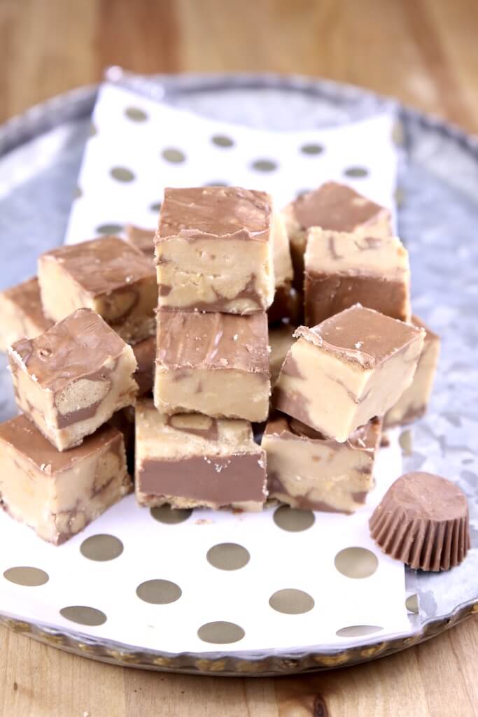 Pieces of peanut butter cup fudge stacked on a black and white polka dot napkin on a blue plate.