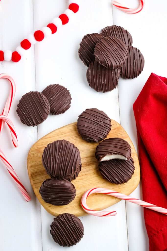 Homemade peppermint patty candies on a wooden cutting board surrounded by candy canes and a red cloth.