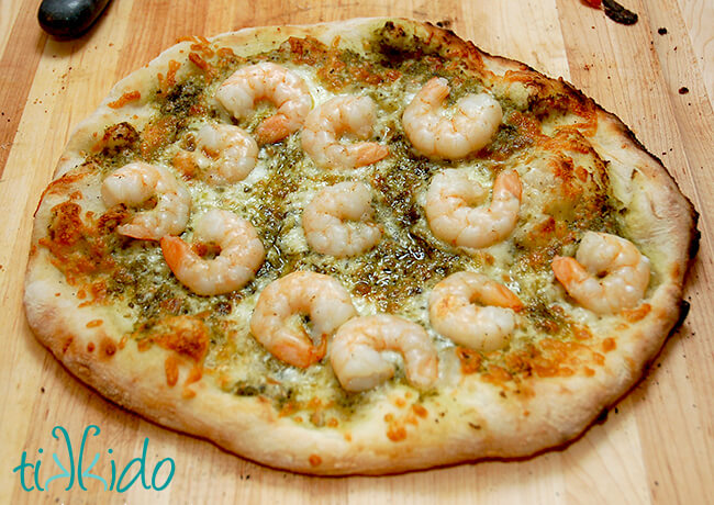 Shrimp and pesto pizza on a wooden cutting board.