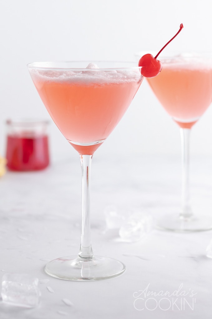 Pink Lady cocktail in a martini glass garnished with a maraschino cherry.