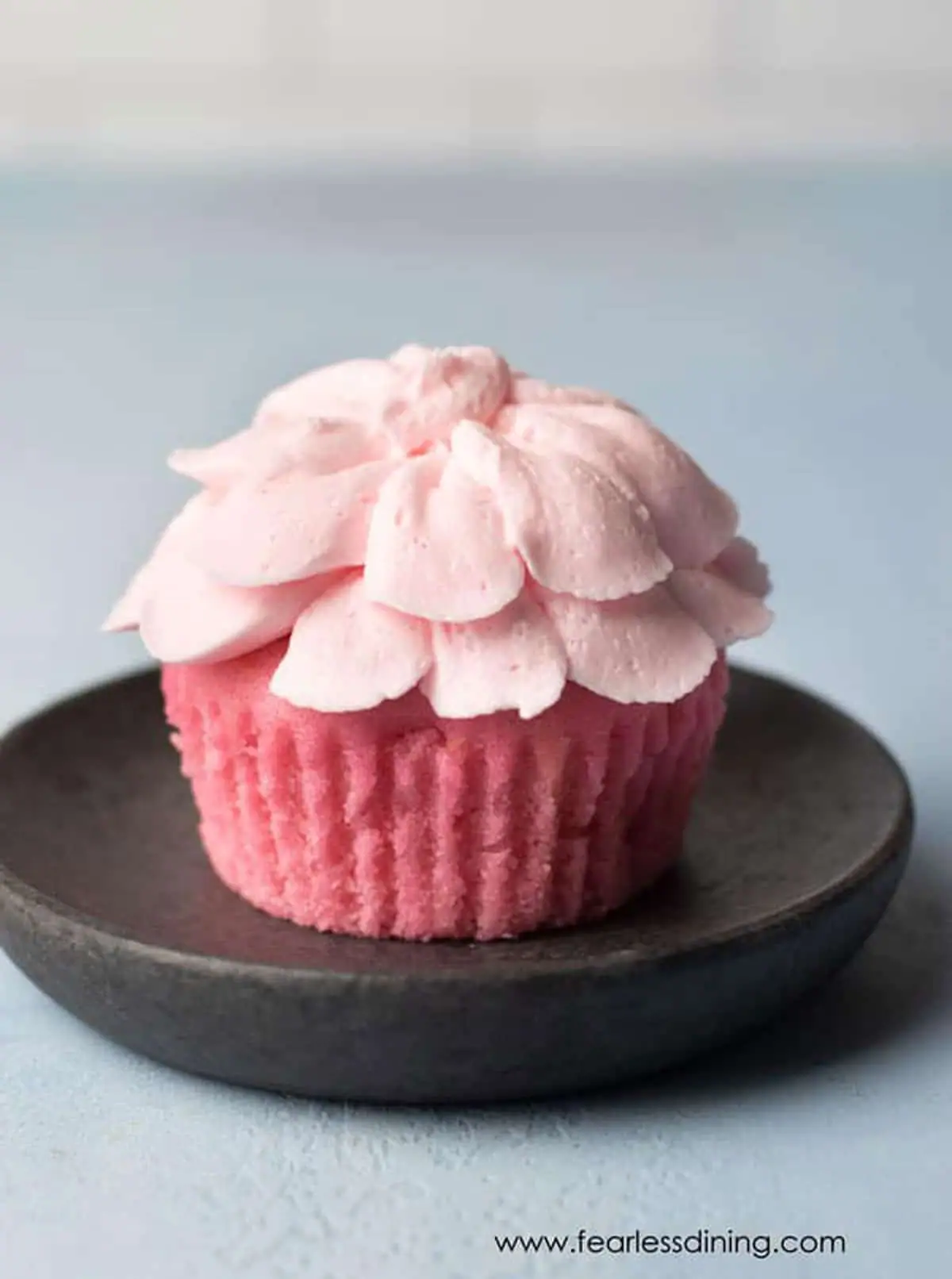 Gluten free pink lemonade cupcake on a small black plate.