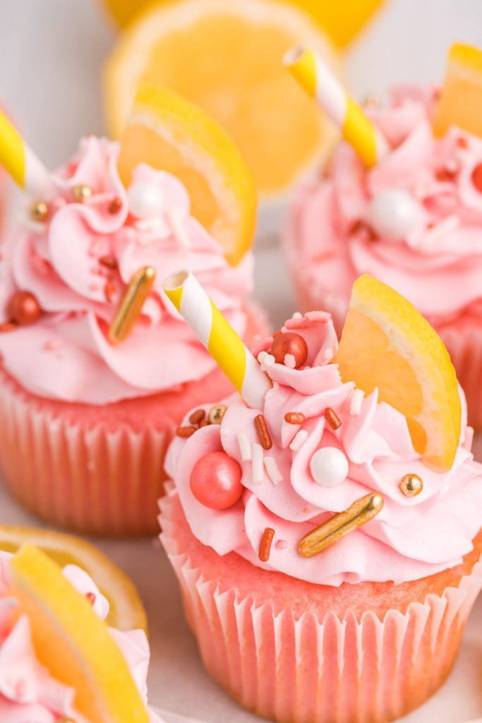 Pink lemonade cupcakes decorated with a slice of lemon and a yellow and white striped paper straw.