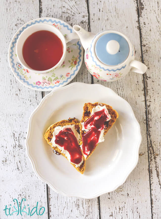 Pumpkin Scones topped with clotted cream and cranberry butter, next to a teapot and cup of tea.