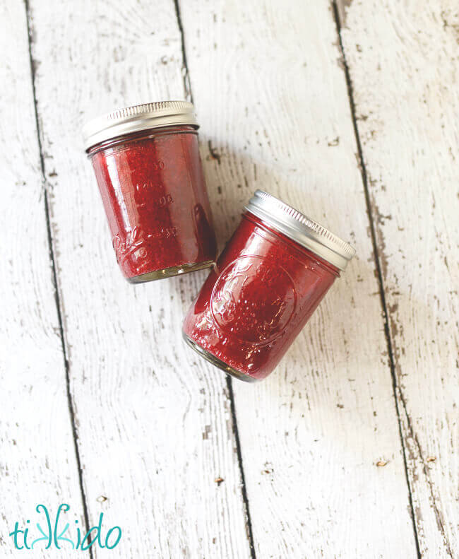 Cranberry butter in two glass canning jars on a weathered white wood background.