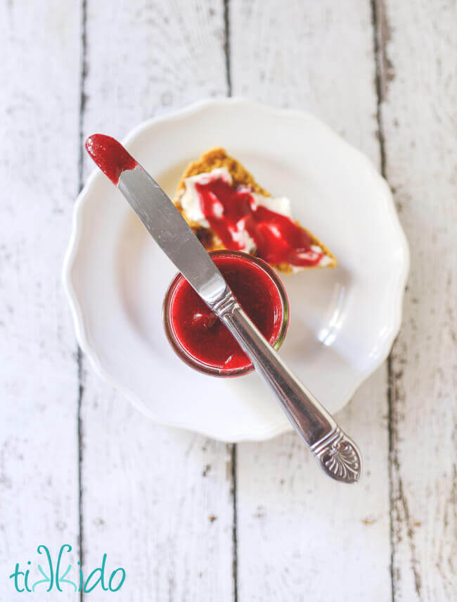 Knife smeared with cranberry butter resting on top of a jar of cranberry butter.