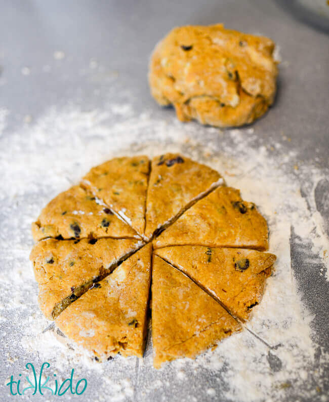 Pumpkin Scones with dried cranberries dough cut into wedge shapes on a floured surface.