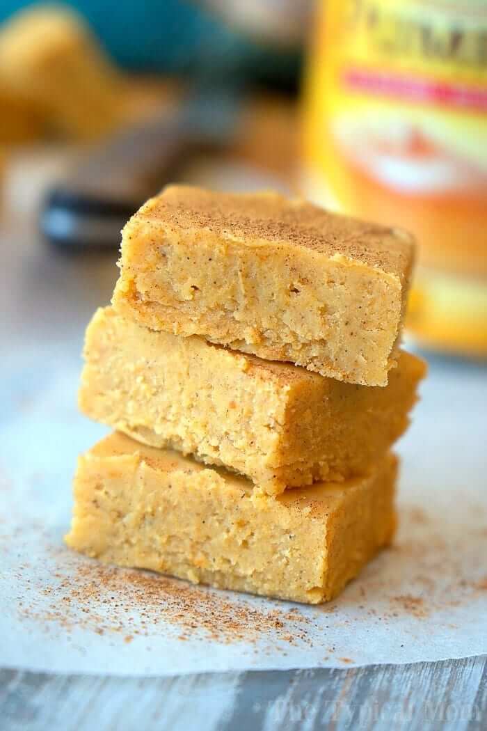 Three pieces of pumpkin fudge stacked on parchment paper and sprinkled with pumpkin spice mix.