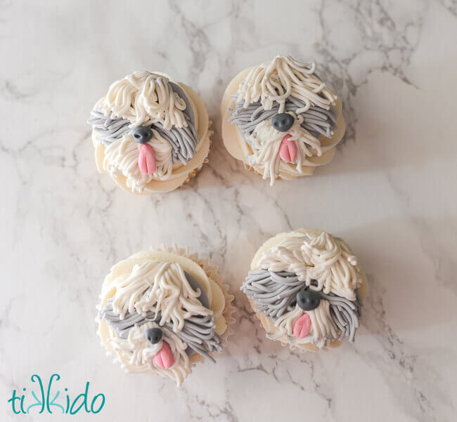 Four cupcakes decorated with gum paste old english sheep dogs.