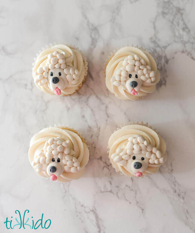 Four cupcakes decorated with gum paste white poodles