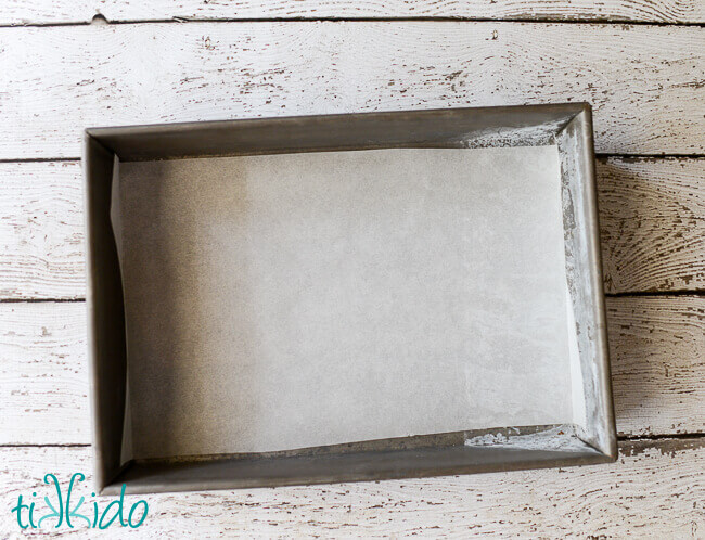 Empty 9x13 cake pan lined with parchment paper on a white wooden background