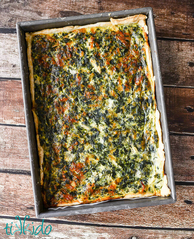 large spinach quiche baked in a 9x13 cake pan, against a weathered wood background.