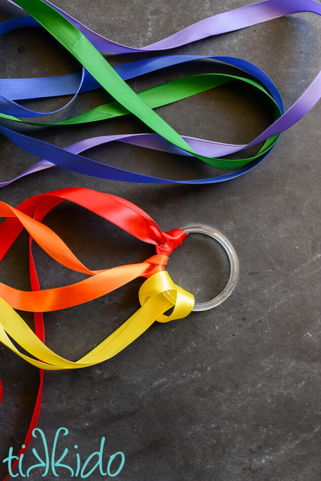 Rainbow colored ribbons being tied on a shower ring to make easy DIY Rainbow Ribbon Toys.