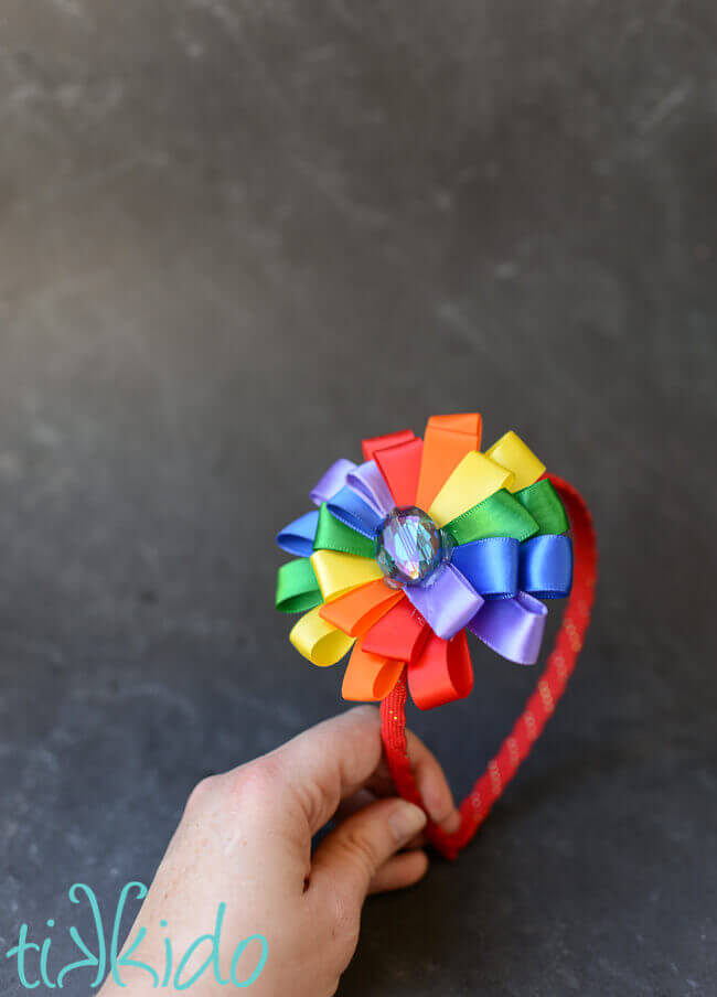 Hand holding a DIY headband made with a rainbow ribbon flower.