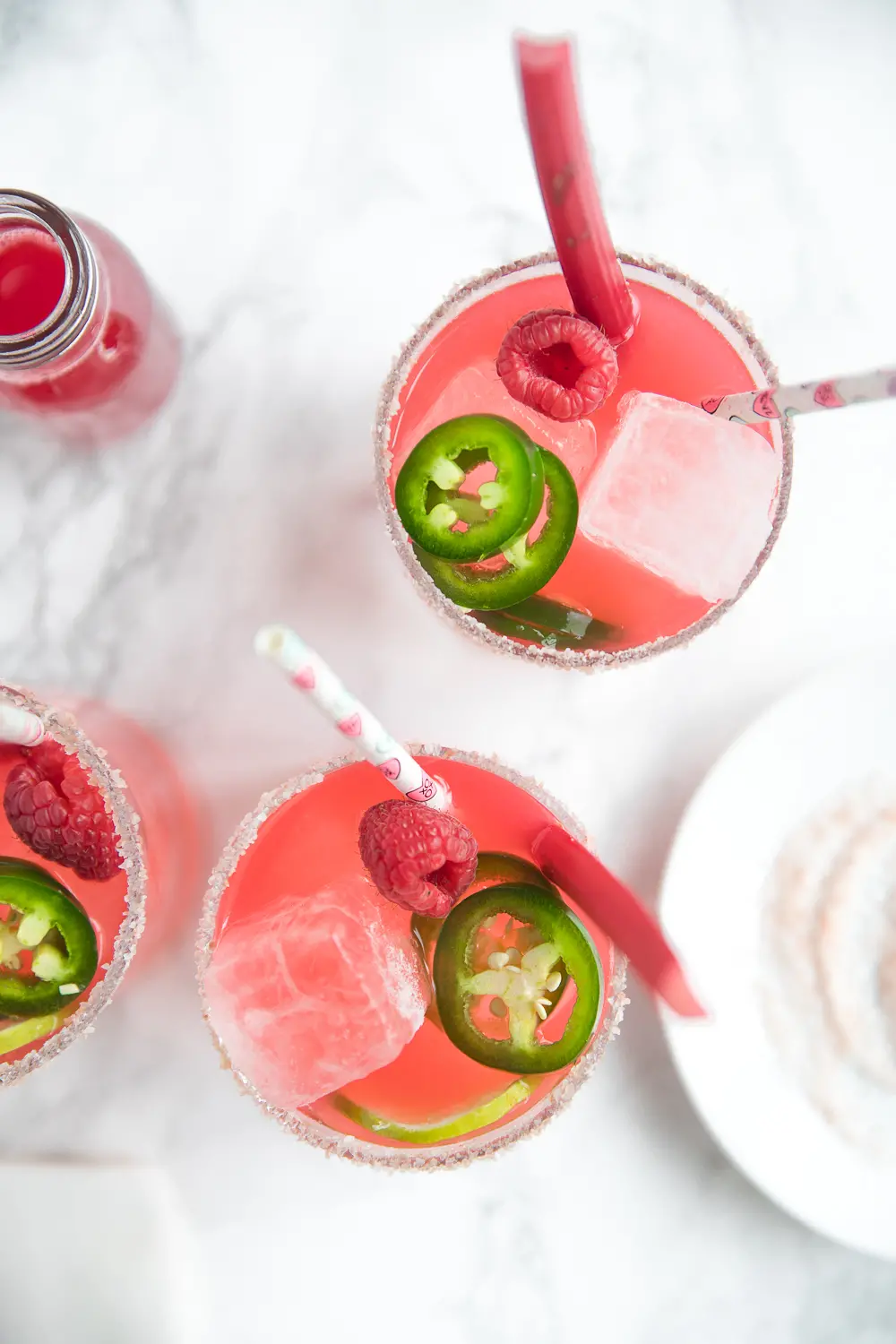 Deep pink raspberry rhubarb margaritas garnished with fresh rhubarb, jalapeños, and raspberries.