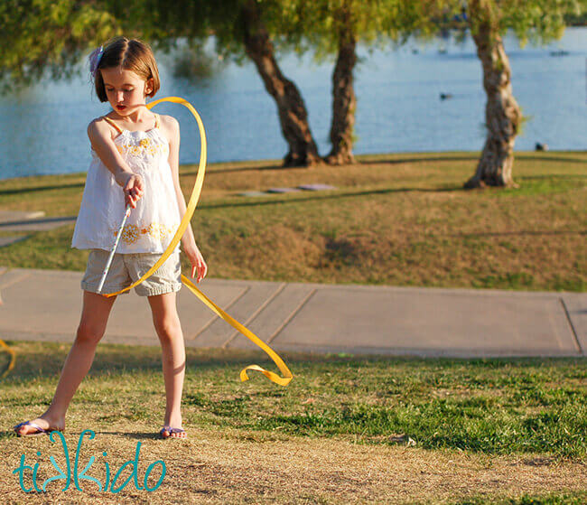 Little girl playing with a yellow ribbon wand in a park.