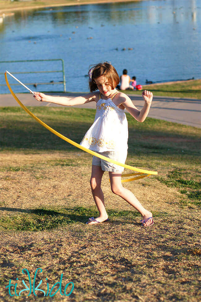 Little girl playing with a yellow ribbon wand in a park.