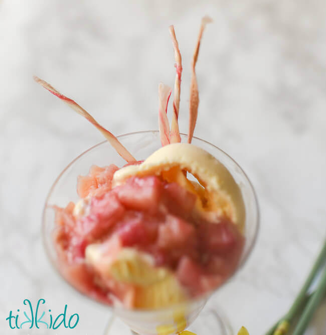 Four strips of candied rhubarb in a glass dish with vanilla ice cream and roasted rhubarb compote.