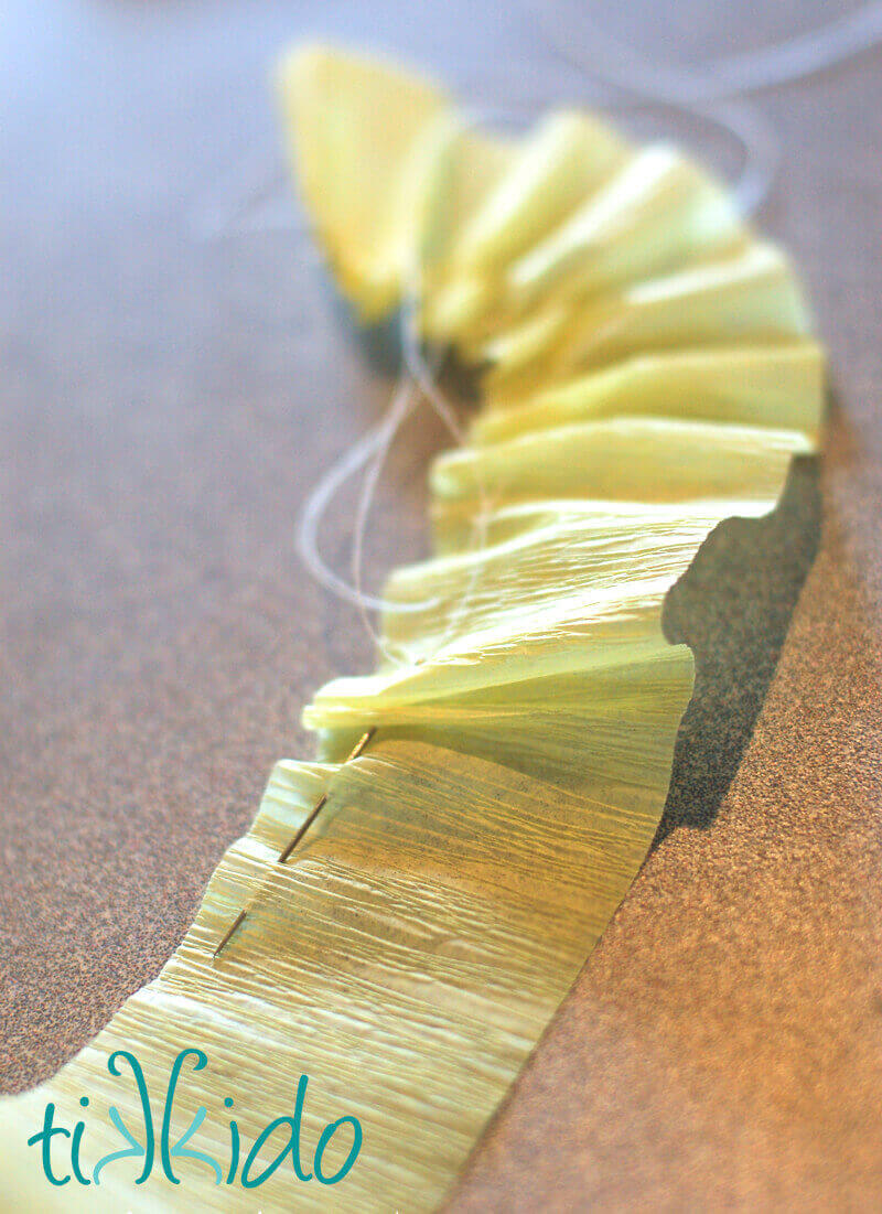 Light yellow crepe paper being gathered into ruffles with needle and thread.