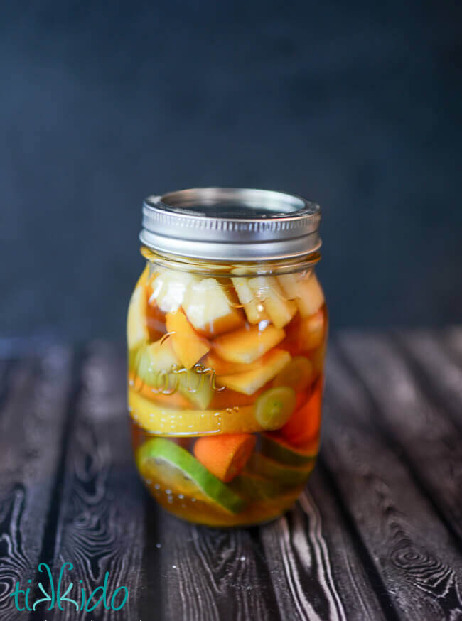 Fruit for White Sangria Recipe in mixture of peach schnapps and brandy in a mason jar.