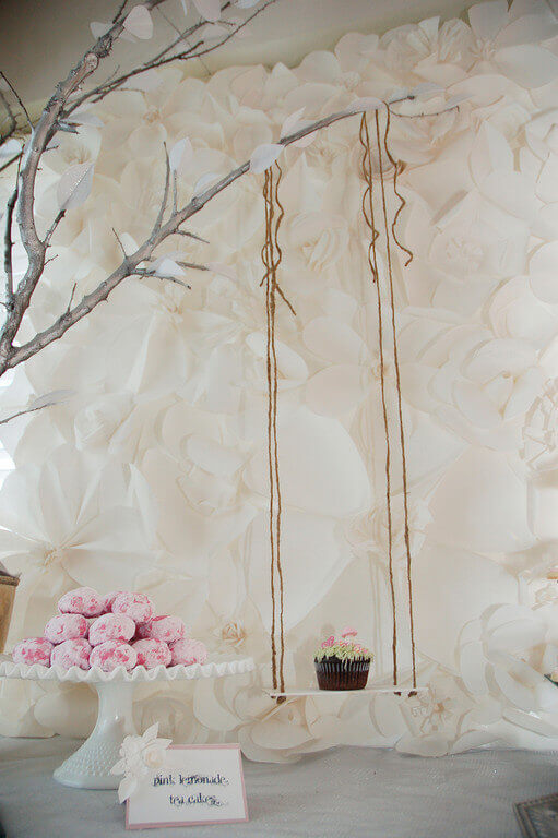 Cupcake on a rustic swing hanging in front of a monochromatic white giant paper flower backdrop.
