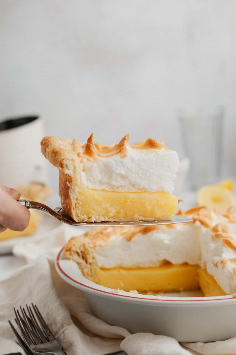 Slice of lemon meringue pie being lifted out of a pie tin with a pie server.