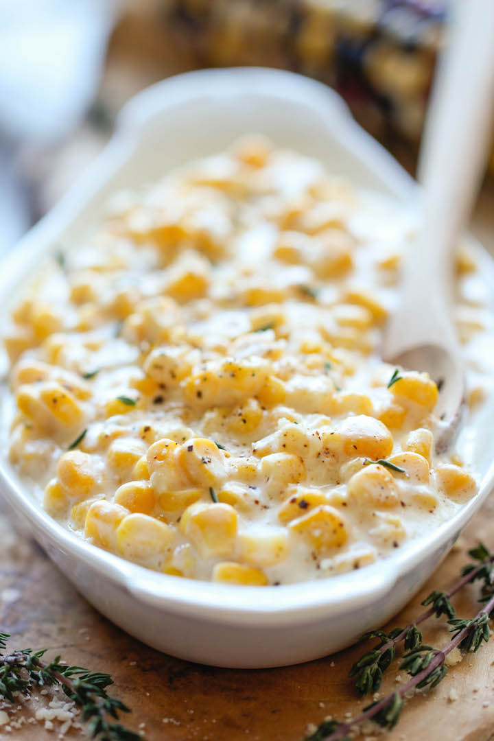 White oval dish filled with slow cooker creamed corn, surrounded by sprigs of fresh thyme.