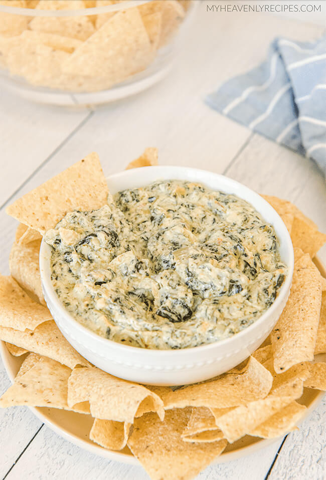 Bowl of crockpot spinach and artichoke dip surrounded by tortilla chips.