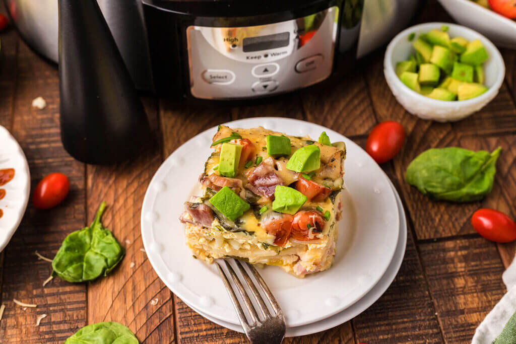 Slice of savory overnight slow cooker breakfast casserole on a white plate, in front of a slow cooker.